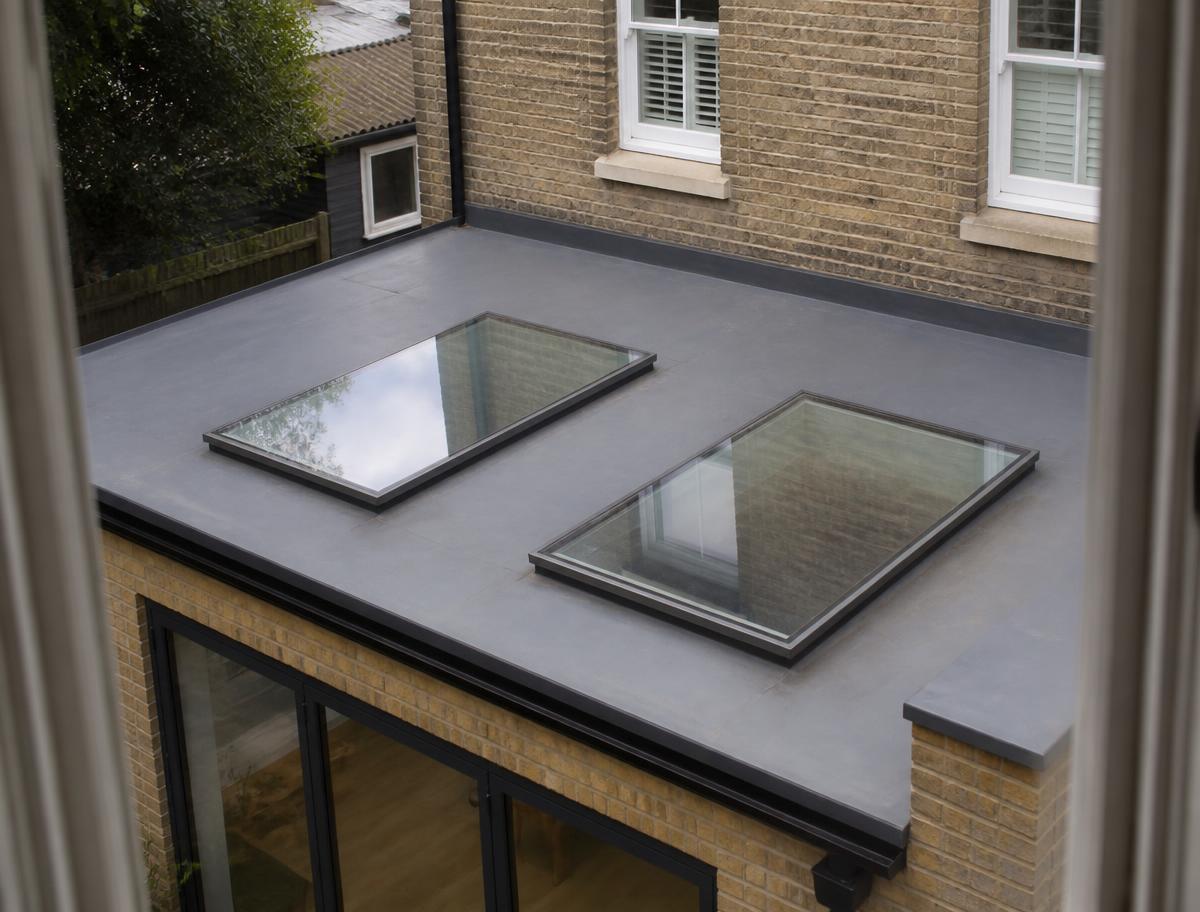 Two flush glass rooflights set into the grey flat roof of a single-storey brick rear extension, seen from an upstairs window